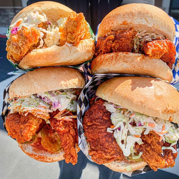 Four Legend Hot Chicken sandwiches with crispy chicken, coleslaw, and pickles on buns.