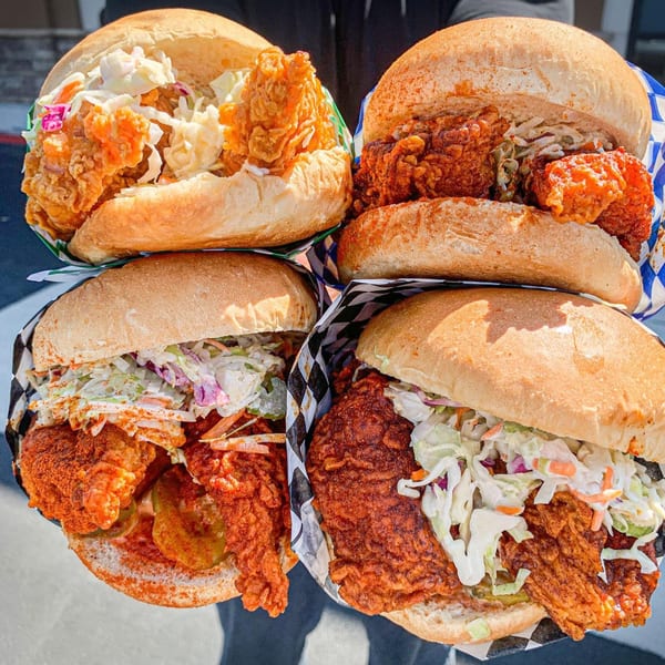 Four Legend Hot Chicken sandwiches, with crispy chicken, coleslaw, and pickles, held by a person.