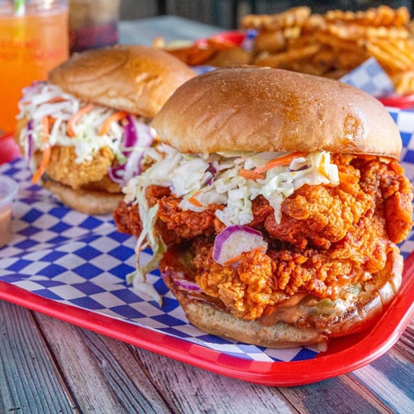 Two Legend Hot Chicken sandwiches with coleslaw and crispy chicken on a red tray with fries.