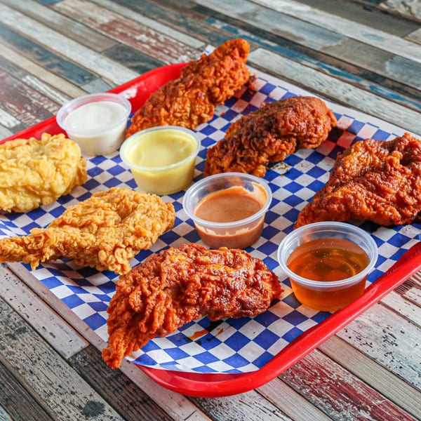 Legend Hot Chicken wings and tenders in various spice levels with dipping sauces on a red tray.