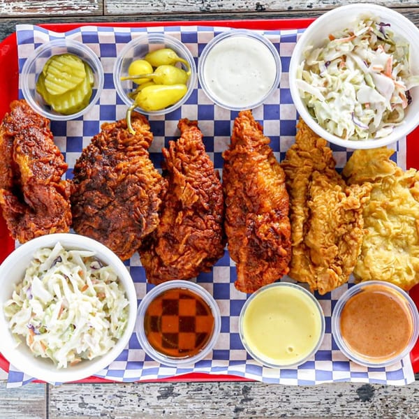 Legend Hot Chicken wings, coleslaw, pickles, peppers, and various dipping sauces on a checkered tray.